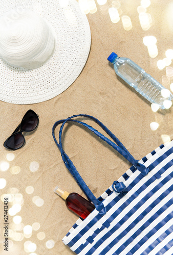 vacation, travel and summer concept - beach bag, sunscreen, sunglasses and hat on sand