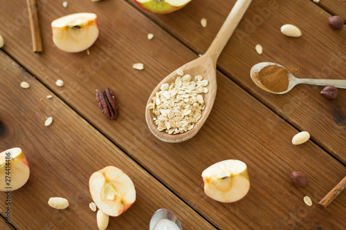 food cooking and eating concept - cut apples, oatmeal in spoon, cinnamon, nuts and sugar on wooden table