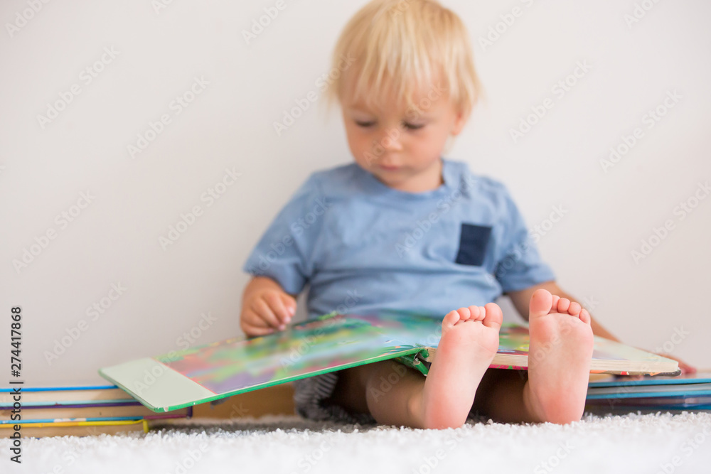 Sweet toddler boy, reading book at home, sitting on the ground, lots of books Sweet toddler boy, reading book at home, sitting on the ground, lots of books