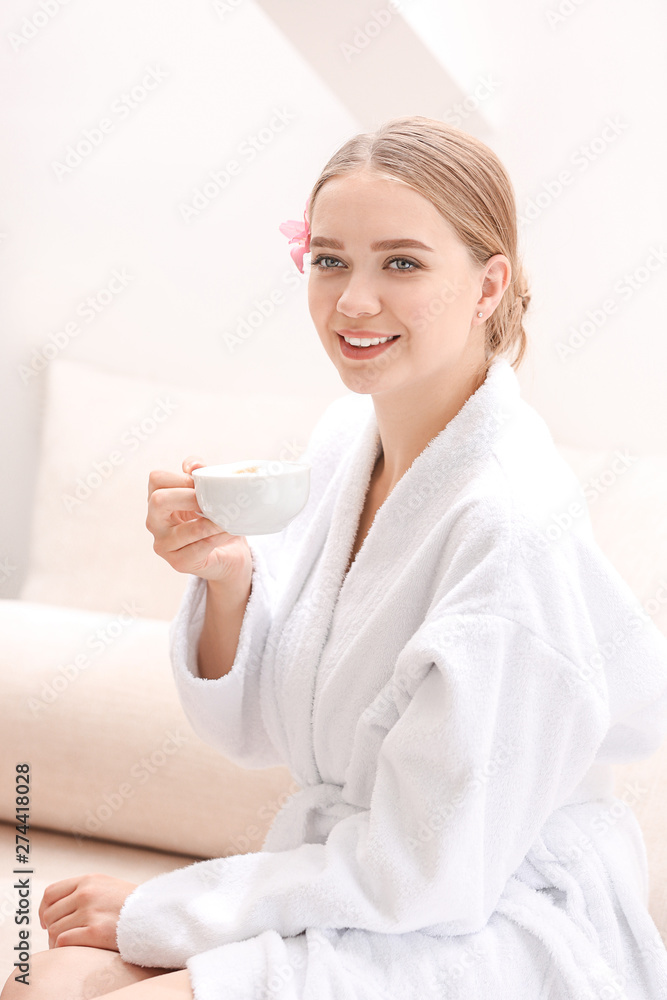 Beautiful young woman drinking coffee in spa salon