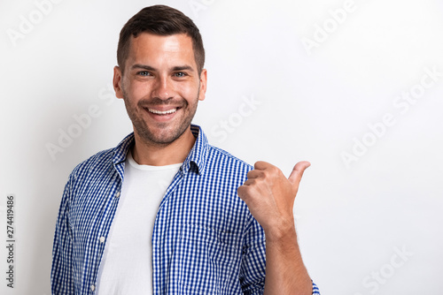 Картината върху платно Handsome happy man pointing by his big finger backward and looking at the camera
