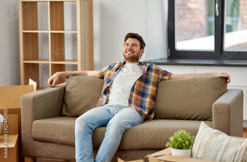 moving, people and real estate concept - happy man with boxes sitting on sofa at new home