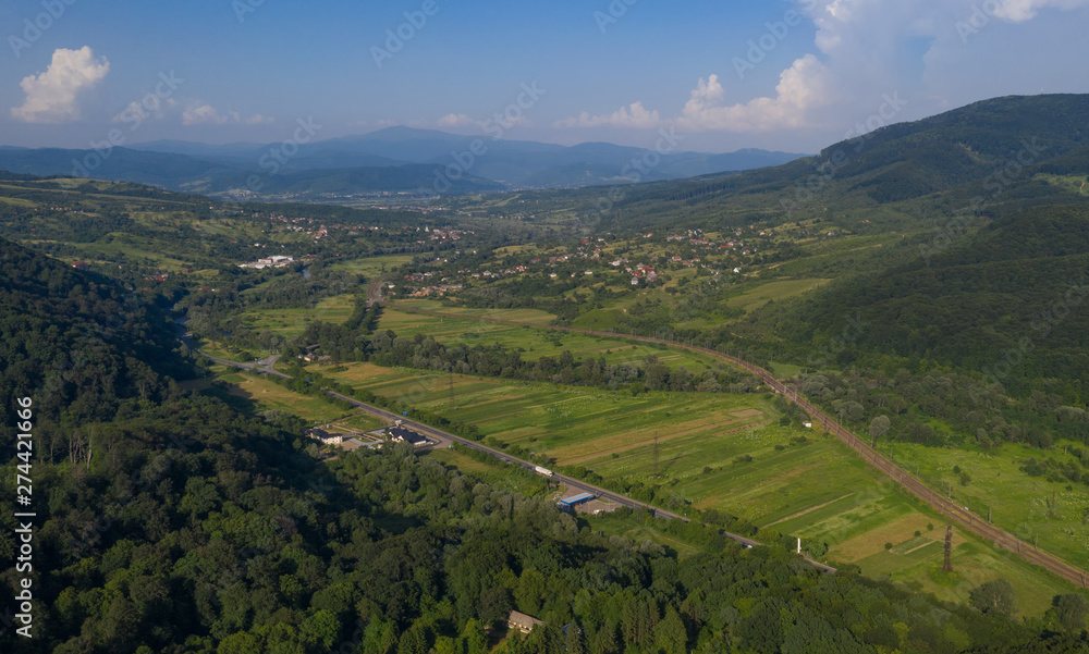 Aerial view of the Carpathian mountains. Natural background with geometric pattern - beige and red rectangles of the fields and roofs and lines of roads and trees. Zakarpattia, Ukraine. Aerial view of the Carpathian mountains. Natural background with geometric pattern - beige and red rectangles of the fields and roofs and lines of roads and trees. Zakarpattia, Ukraine.