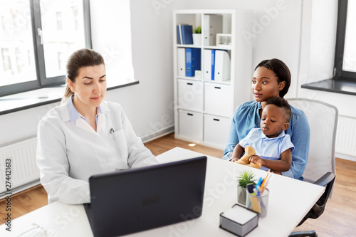 medicine, healthcare and pediatry concept - african american mother with baby son and caucasian doctor with laptop computer at clinic