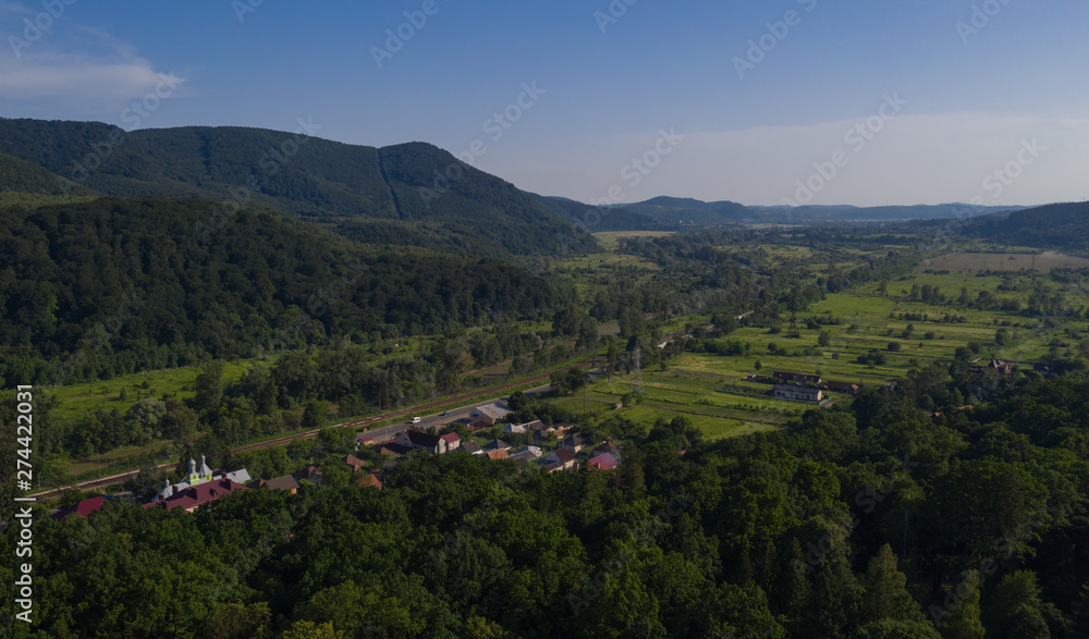 Obraz premium Aerial view of the Carpathian mountains. Natural background with geometric pattern - beige and red rectangles of the fields and roofs and lines of roads and trees. Zakarpattia, Ukraine.