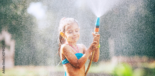 Cute little girl sprinkls a water for herself from the hose  makes a rain. pleasure for hot summer days