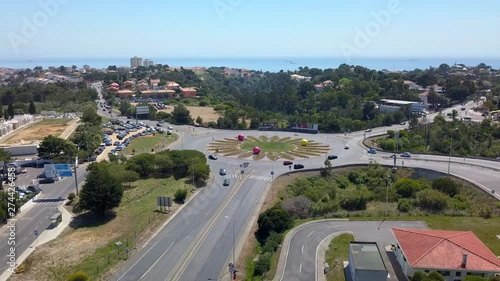 Aerial, drone shot towards a roundabout decorated with large tennis balls, birdseye above cars driving in the traffic circle,  on a sunny day, near Estoril Tennis club, in Portugal photo