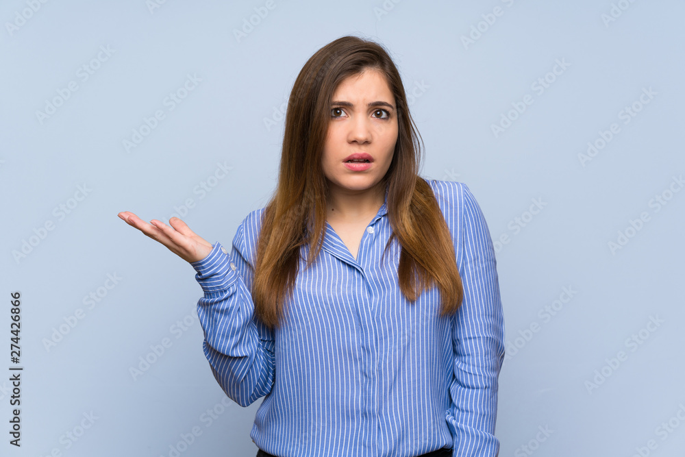 Young girl over isolated blue wall making doubts gesture Young girl over isolated blue wall making doubts gesture