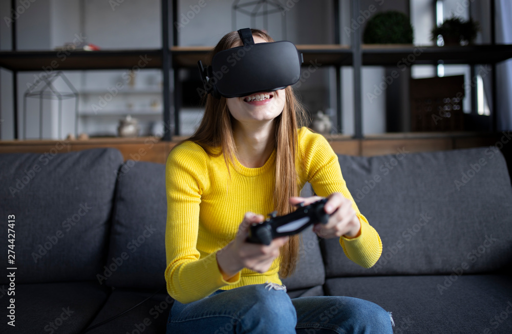 Fototapeta premium Cute girl plays the game on the console. Happy young woman using a virtual reality headset