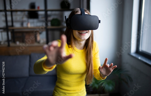Excited girl in a VR glasses surprised. She is touchinmg something and express the emotions from this experience. Wow