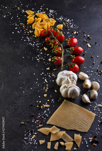 Ingredients for cooking pasta on a black background. Pasta, sherry tomatoes, garlic, cheese, pepper and salt.
