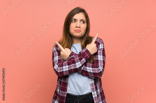 Young girl over pink wall pointing to the laterals having doubts