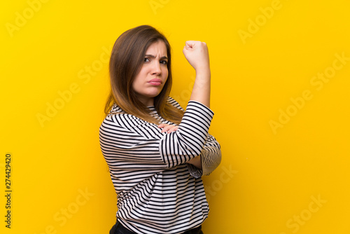 Young girl over yellow wall doing strong gesture