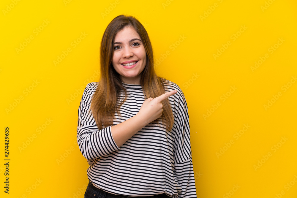 Fototapeta premium Young girl over yellow wall pointing to the side to present a product