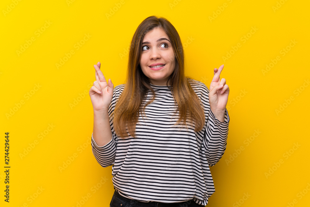 Young girl over yellow wall with fingers crossing and wishing the best Young girl over yellow wall with fingers crossing and wishing the best