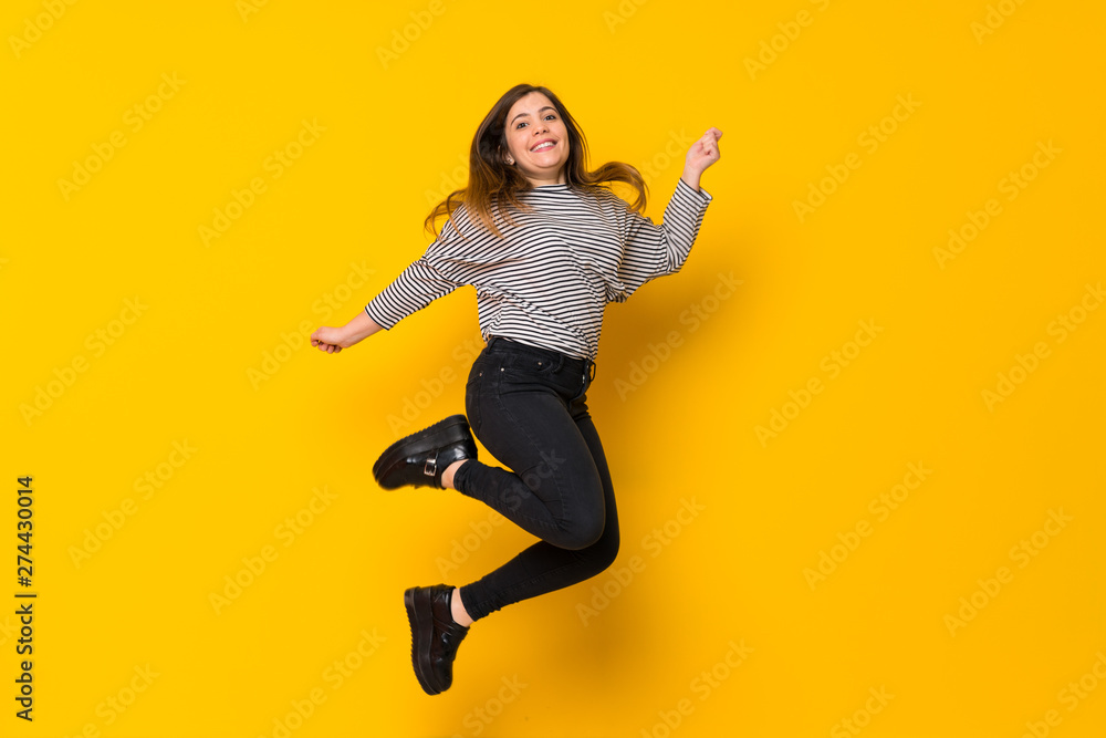 A full-length shot of a Young girl  jumping over isolated yellow background