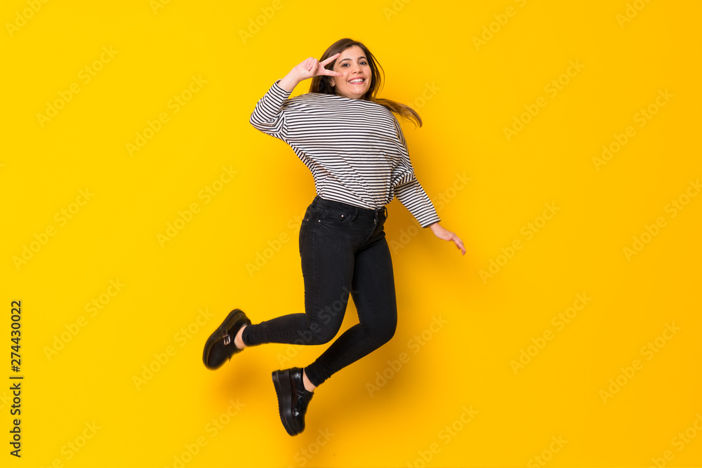 A full-length shot of a Young girl  jumping over isolated yellow background