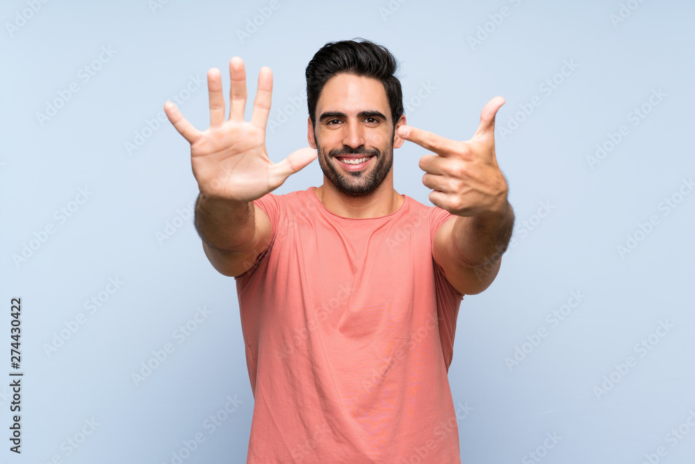 Handsome young man in pink shirt over isolated blue background counting seven with fingers Handsome young man in pink shirt over isolated blue background counting seven with fingers