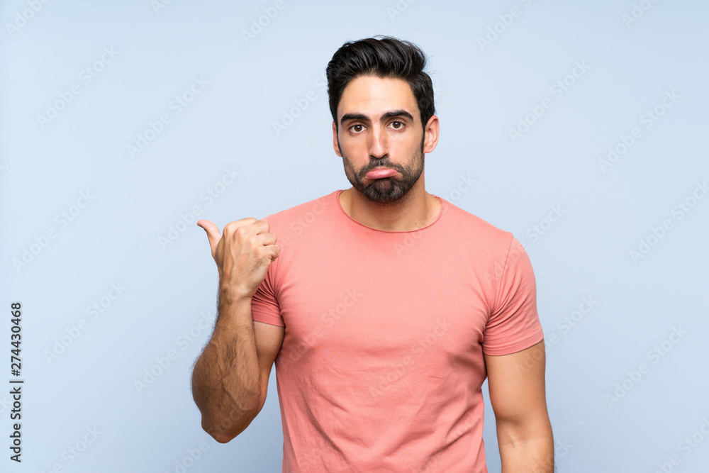 Fototapeta premium Handsome young man in pink shirt over isolated blue background unhappy and pointing to the side