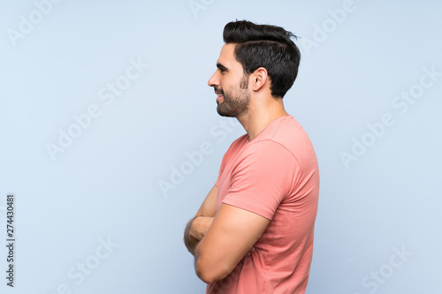 Handsome young man in pink shirt over isolated blue background in lateral position