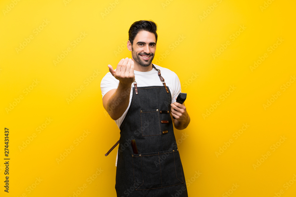 Young hairdresser man over isolated yellow background inviting to come with hand. Happy that you came Young hairdresser man over isolated yellow background inviting to come with hand. Happy that you came