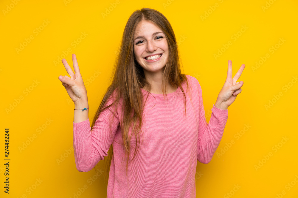 Young woman with long hair over isolated yellow wall showing victory sign with both hands Young woman with long hair over isolated yellow wall showing victory sign with both hands