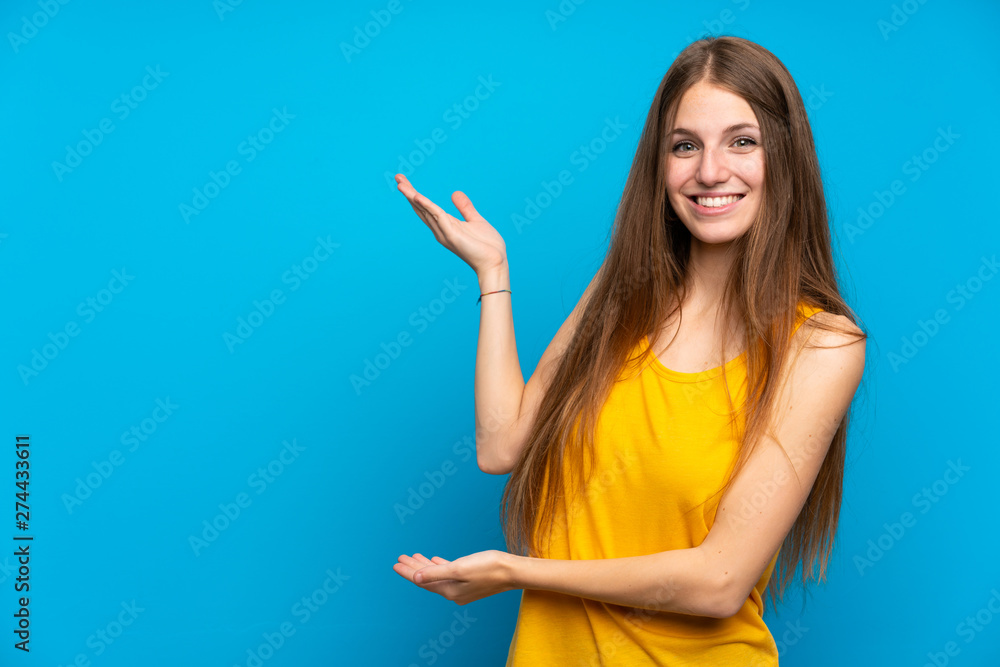 Fototapeta premium Young woman with long hair over isolated blue wall extending hands to the side for inviting to come
