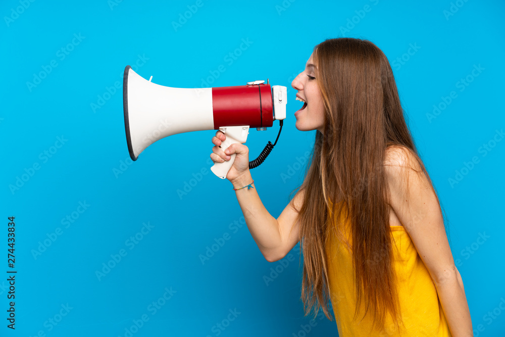 Young woman with long hair over isolated blue wall shouting through a megaphone Young woman with long hair over isolated blue wall shouting through a megaphone