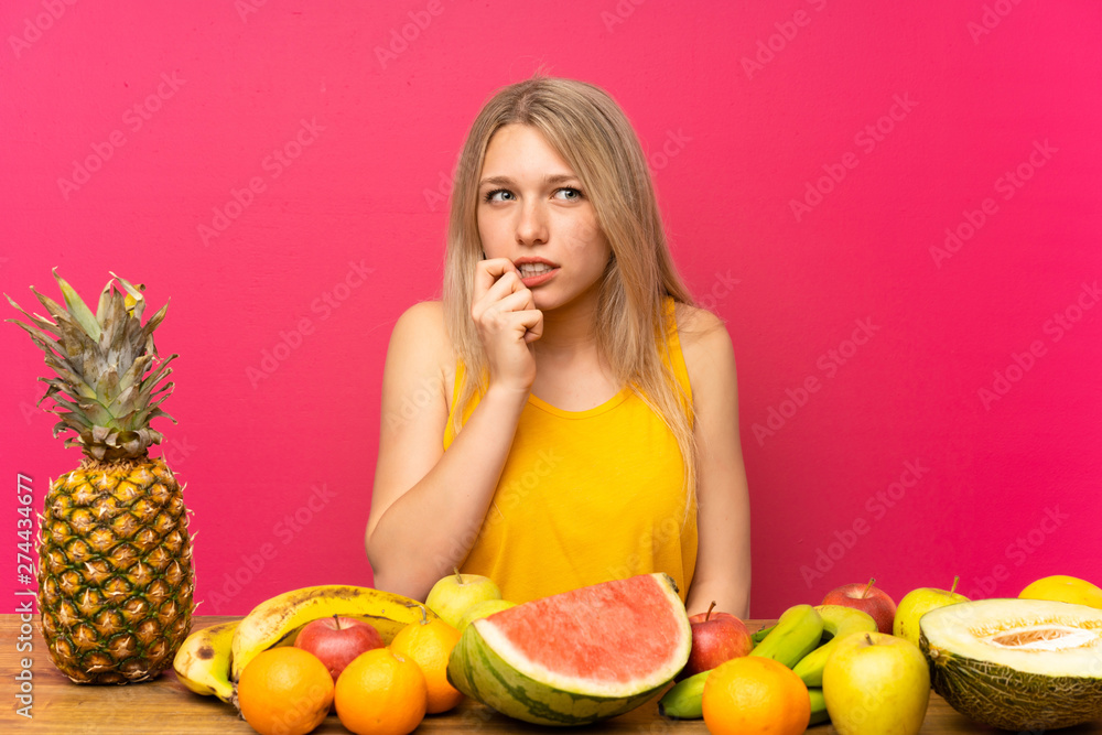 Young blonde woman with lots of fruits nervous and scared Young blonde woman with lots of fruits nervous and scared
