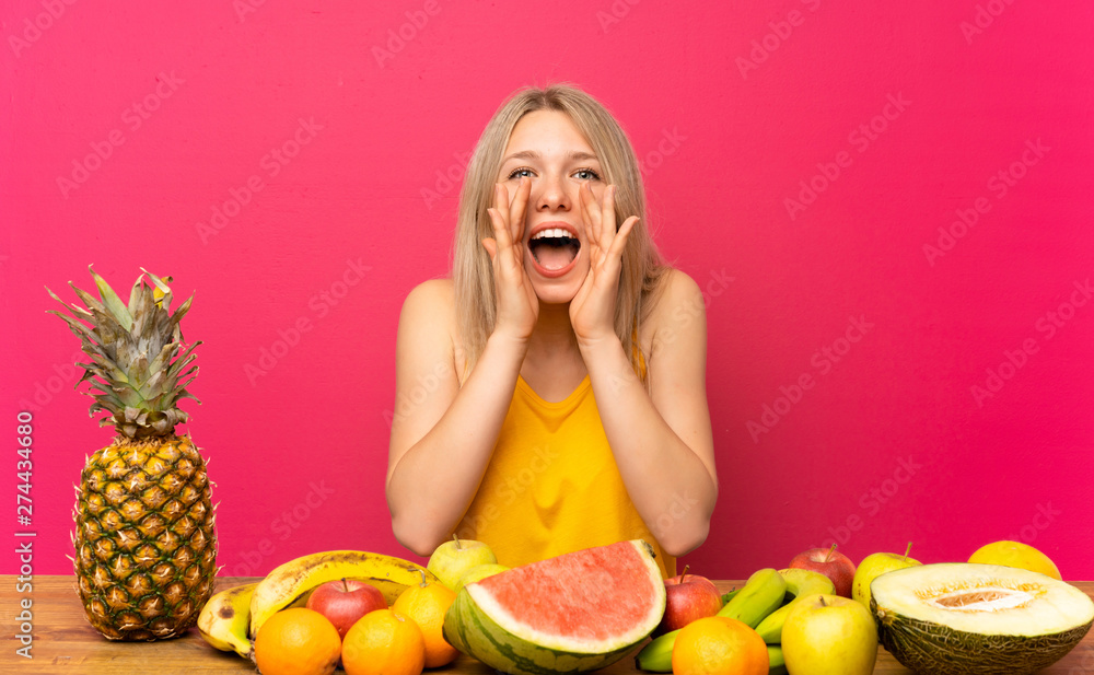 Young blonde woman with lots of fruits shouting with mouth wide open