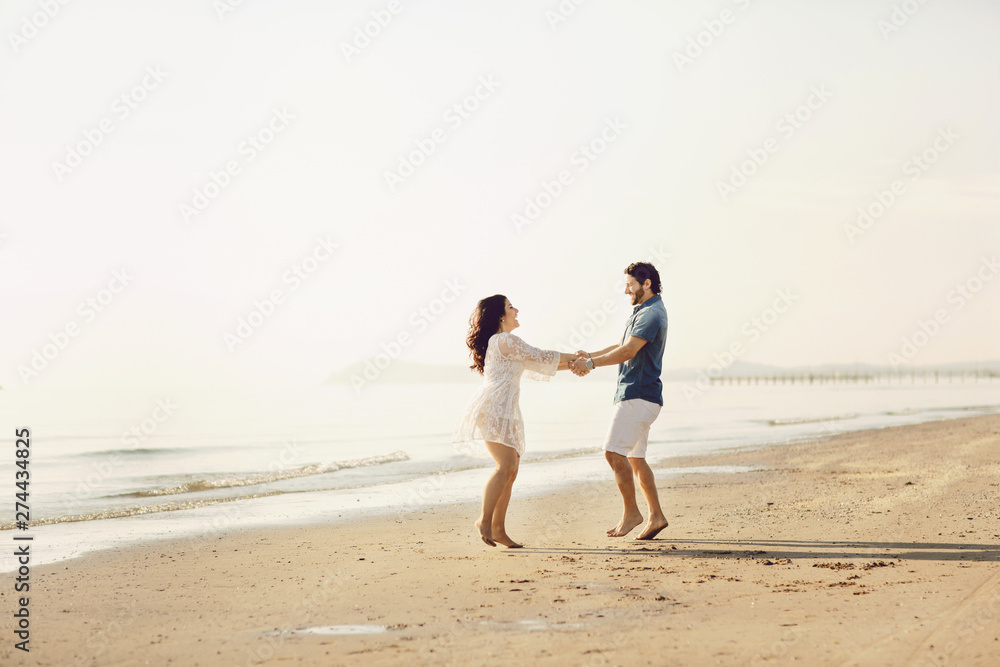 Happy couple in love has fun on the beach. They jump, laugh and enjoy the sea