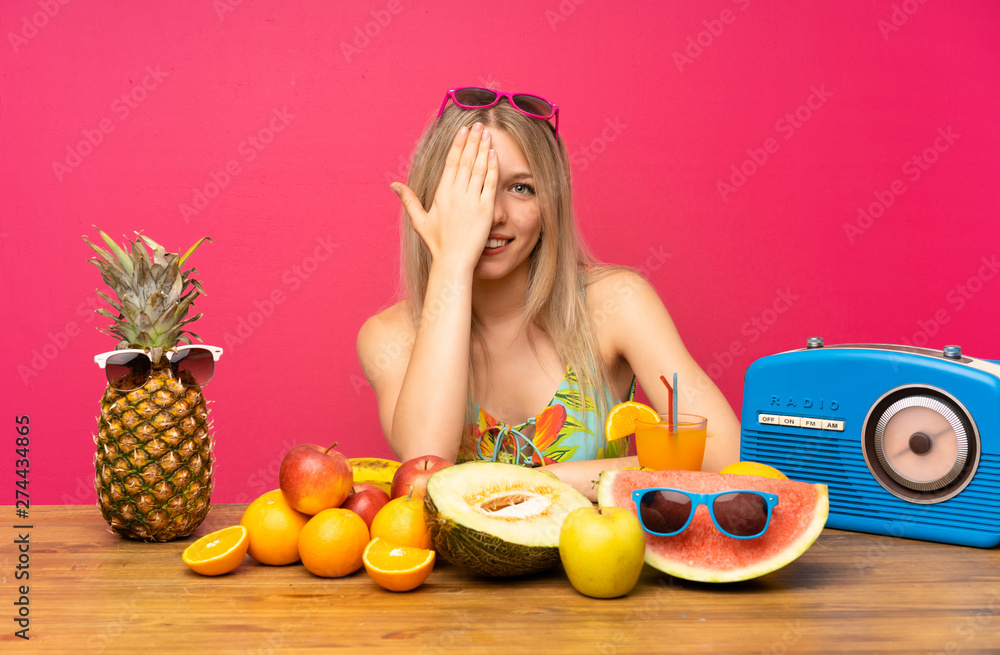 Young blonde woman with lots of fruits covering a eye by hand Young blonde woman with lots of fruits covering a eye by hand