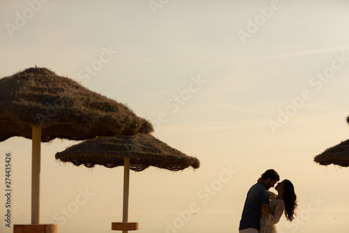 Couple in love having romantic tender moments on the beach near wicker umbrellas. Young lovers enjoying summer vacation © Olha