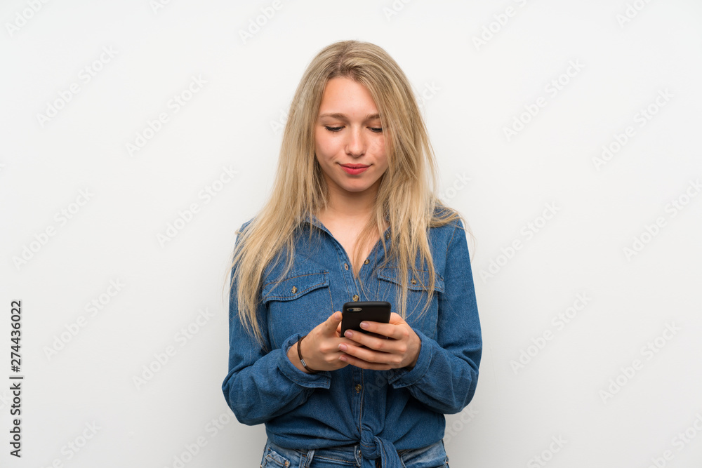 Young blonde woman over isolated white wall sending a message with the mobile Young blonde woman over isolated white wall sending a message with the mobile