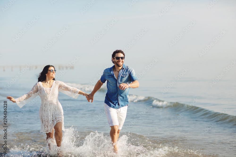 Happy couple walking and playing on the beach, soaking his feet in the water. Wonderful love story in Rimini, Italy Happy couple walking and playing on the beach, soaking his feet in the water. Wonderful love story in Rimini, Italy