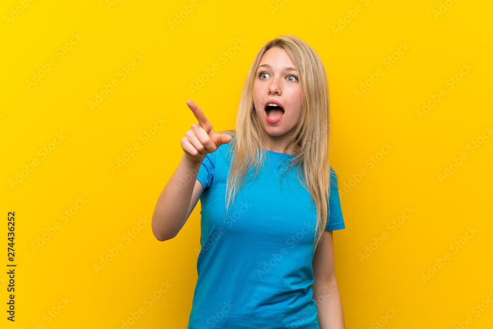 Young blonde woman over isolated yellow background pointing away Young blonde woman over isolated yellow background pointing away