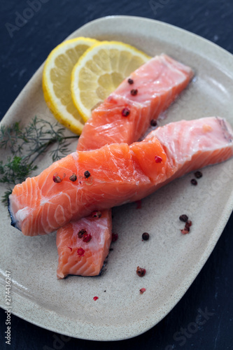 raw salmon with dill and lemon on white dish on ceramic background