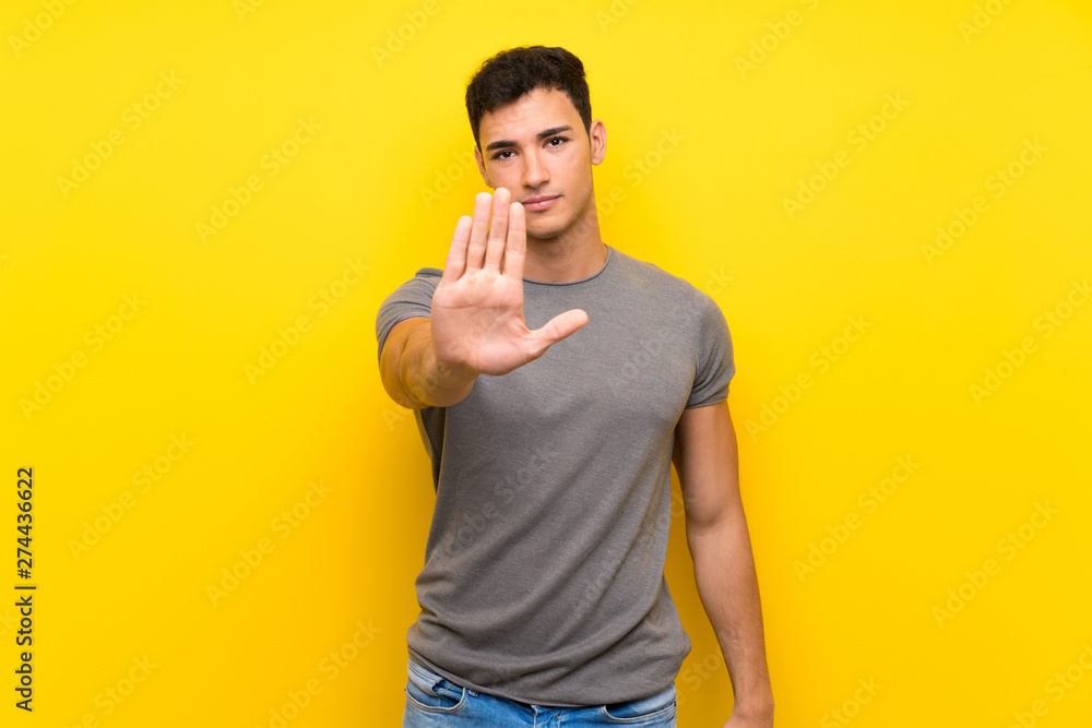 Handsome man over isolated yellow wall making stop gesture Handsome man over isolated yellow wall making stop gesture
