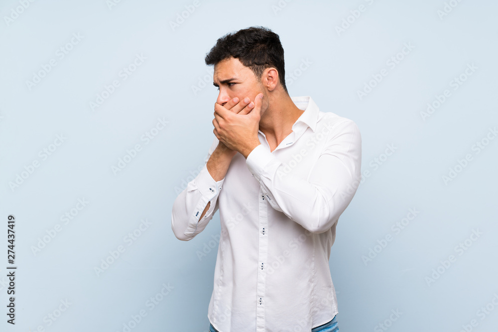 Handsome man over blue wall covering mouth and looking to the side Handsome man over blue wall covering mouth and looking to the side