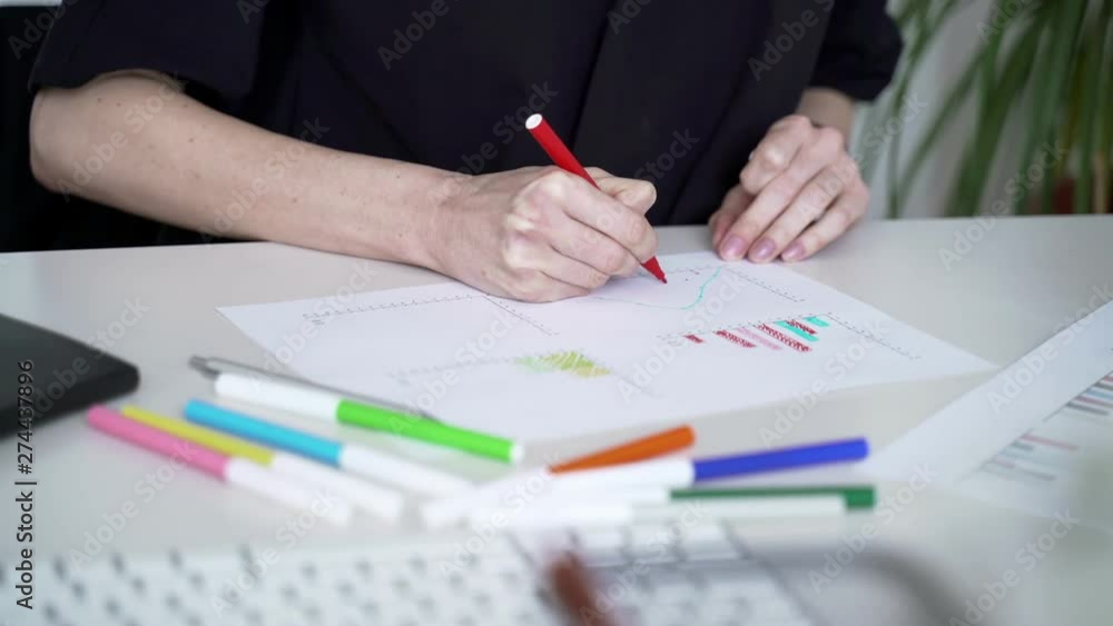 Woman fills data in graphs on paper. Records information. Woman is engaged in office work. Graphic charts,indicators. Woman works at the offside table. Woman draws symbols on the paper Woman fills data in graphs on paper. Records information. Woman is engaged in office work. Graphic charts,indicators. Woman works at the offside table. Woman draws symbols on the paper