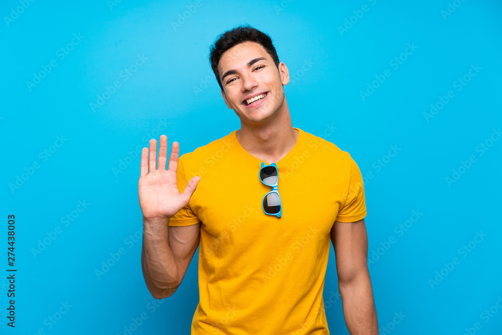 Handsome man over blue background saluting with hand with happy expression Handsome man over blue background saluting with hand with happy expression