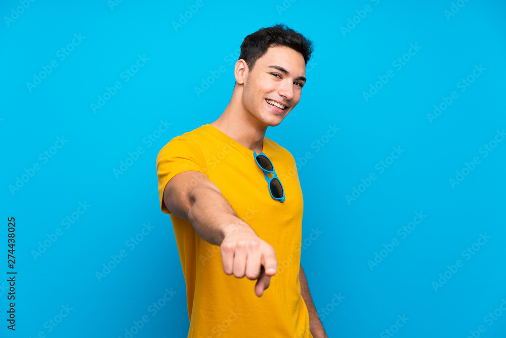 Handsome man over blue background points finger at you with a confident expression Handsome man over blue background points finger at you with a confident expression