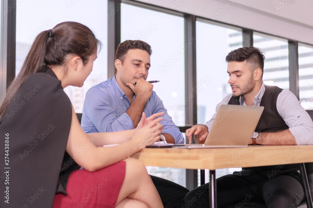 Group businesspeople colleagues talking about planning project in the workplace. Man holding pen with colleagues sitting on desk with laptop while talking work together in office on city background. Group businesspeople colleagues talking about planning project in the workplace. Man holding pen with colleagues sitting on desk with laptop while talking work together in office on city background.
