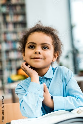 selective focus of cheerful african american kid smiling near book on table