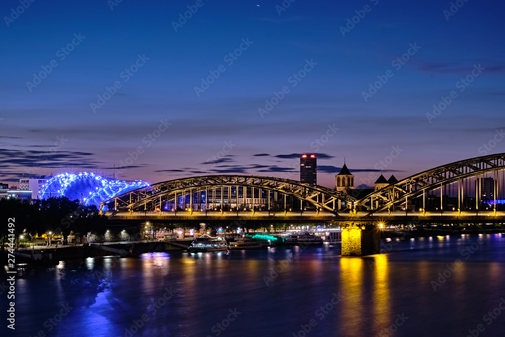 Musical Dome und Hohenzollernbrücke in Köln, Blick über den Rhein während der blauen Stunde bei Nacht.
