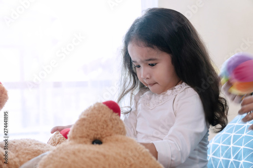 Cheerful cute little girl playing big brown teddy bear sitting on bed in bedroom. Lifestyle child relaxation concept
