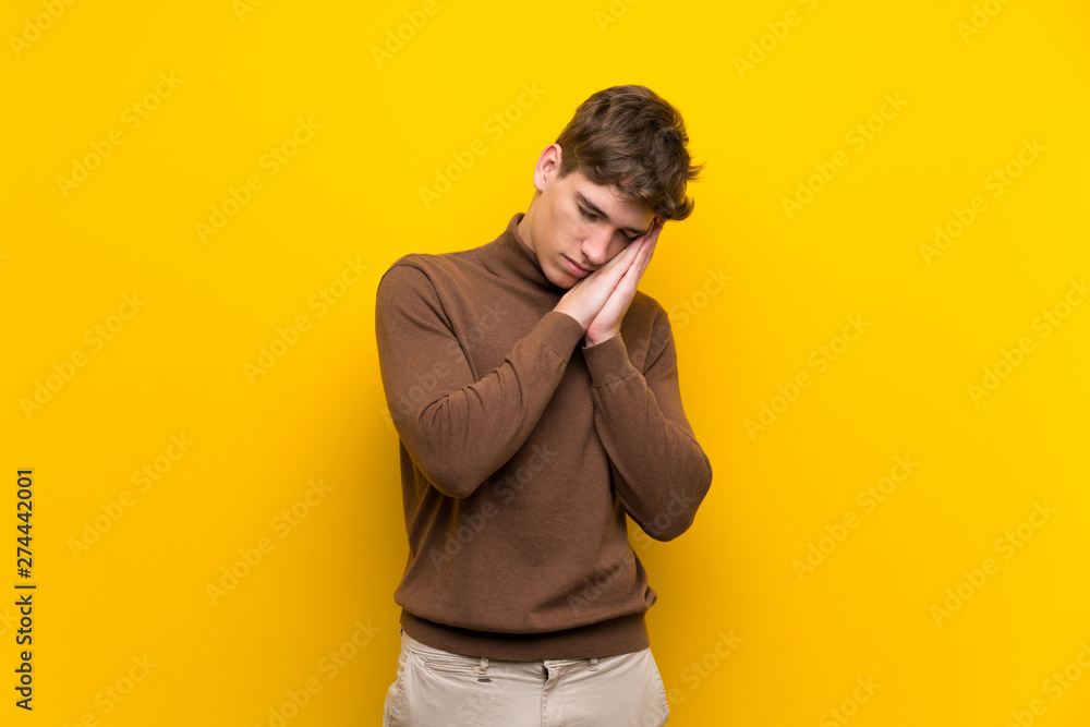 Handsome young man over isolated yellow background making sleep gesture in dorable expression Handsome young man over isolated yellow background making sleep gesture in dorable expression