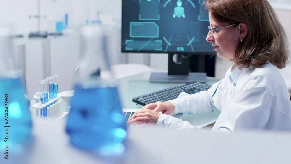 Handheld shot of scientist woman typing on laptop at her desk Handheld shot of scientist woman typing on laptop at her desk