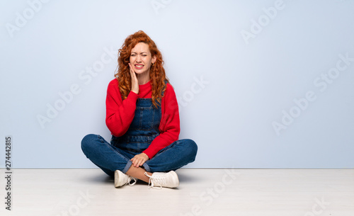 Redhead woman with overalls sitting on the floor with toothache