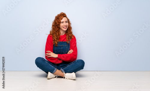 Redhead woman with overalls sitting on the floor with arms crossed and looking forward